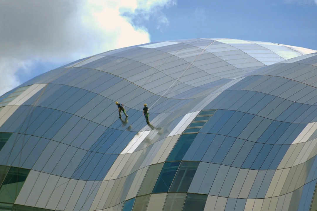 Two workers cleaning windows on a glass building facade using a lift platform, enhancing building aesthetics.