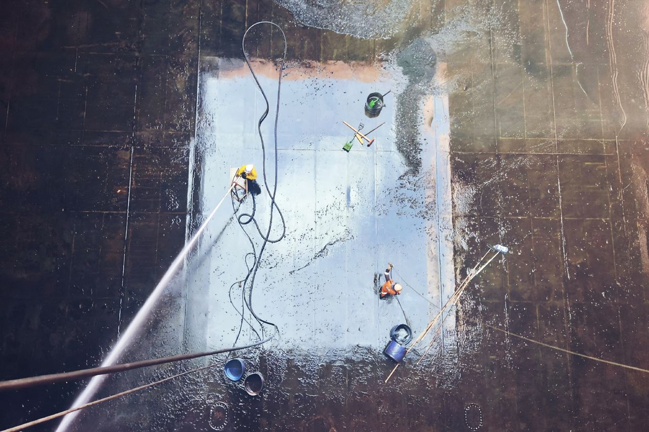 Vue aérienne de techniciens effectuant le nettoyage d'une vaste surface à l'aide d'équipements et de tuyaux d'eau.