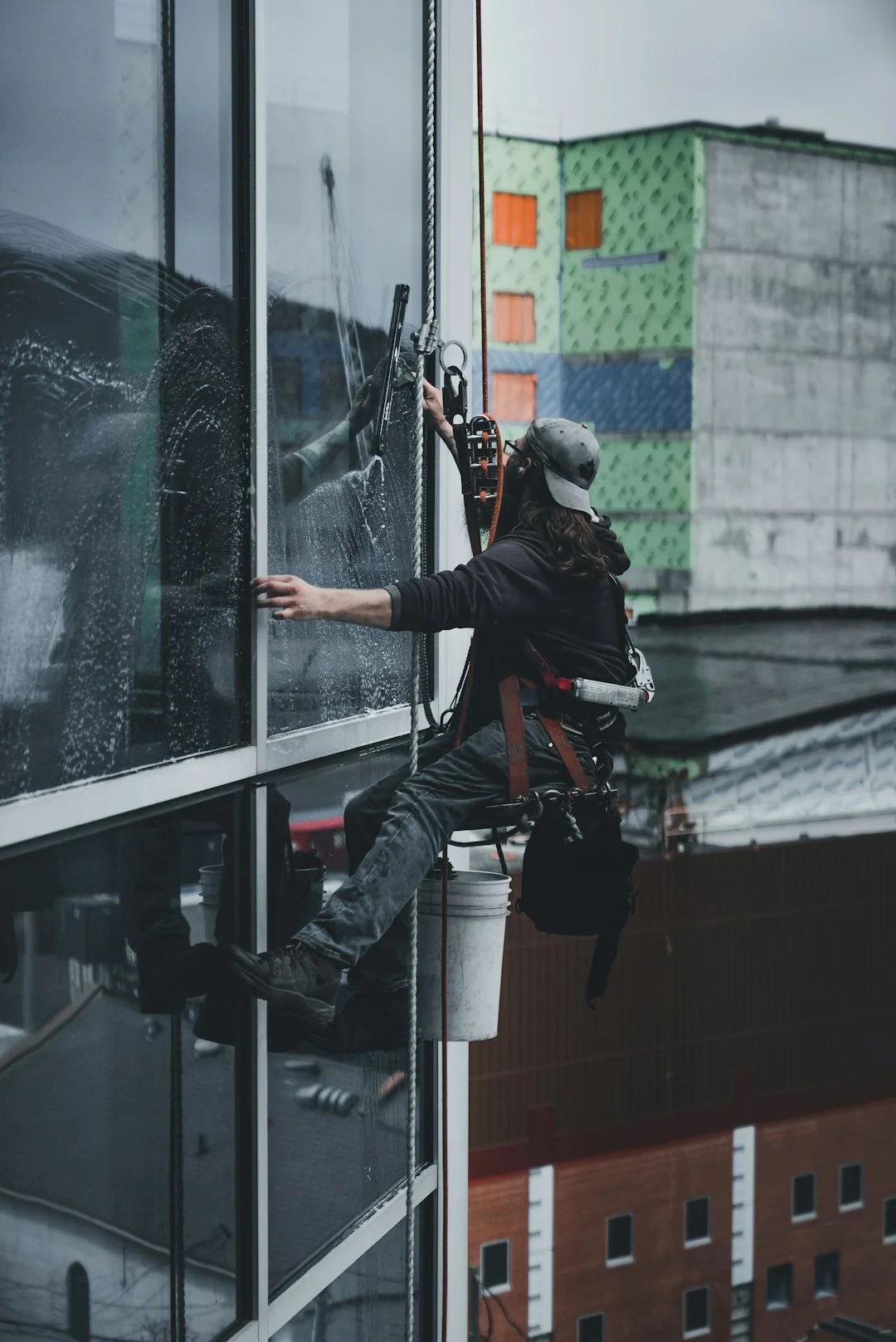 Two workers clean windows on a modern glass building facade using a suspended platform.